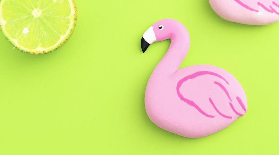 A rock painted in the color of a flamingo on a green background.