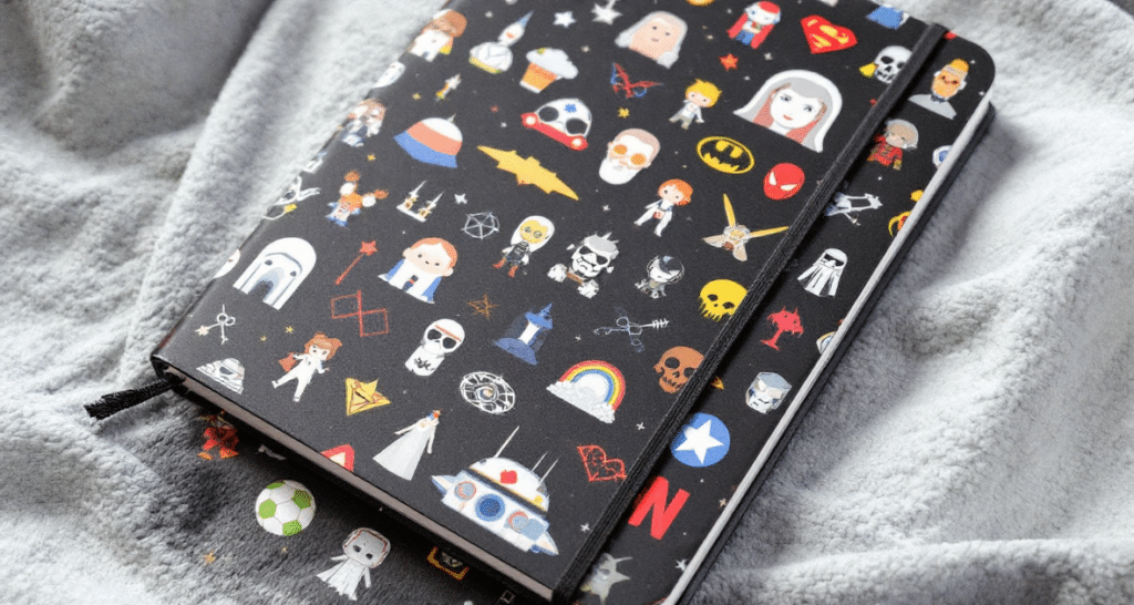 A close-up photo of a notebook with a unique, cartoon-like design featuring a variety of pop culture icons against a black background.