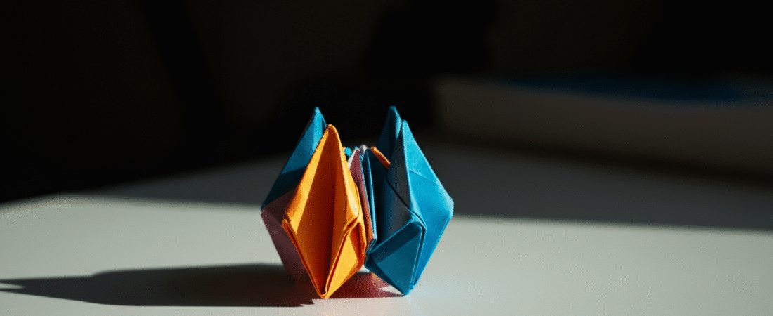 Colorful blue orange origami simply paper crafts Photograph of two vibrant intricately folded origami objects one orange and one blue standing on a light surface with dramatic shadows against a dark background highlighting craftsmanship and creative potential