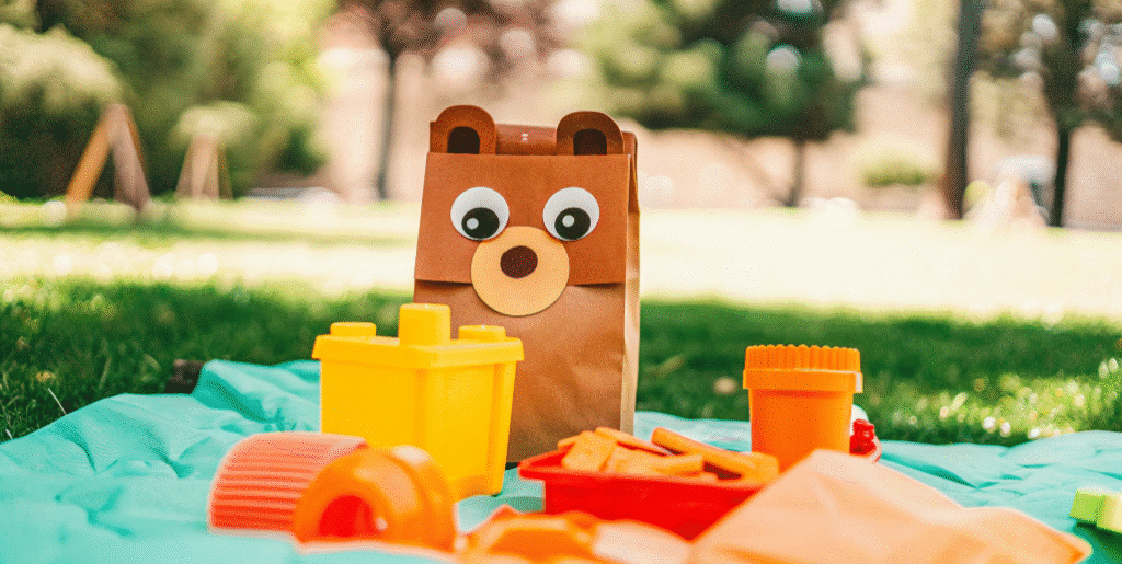 Picnic bear puppet simply paper crafts The image features a playful scene of a bear paper bag puppet sitting on a picnic blanket surrounded by colorful snacks and toys representing a fun teddy bear picnic This adorable bear puppet made from simple materials like construction paper and googly eyes invites creativity and imagination for kids and families alike
