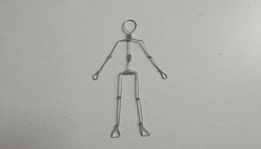 Image The image depicts a simple wire stick figure armature for a human form lying flat on a work surface Constructed from aluminum wire this armature serves as the foundational structure for a paper mache sculpture ready to be covered with layers of materials like tin foil and paper