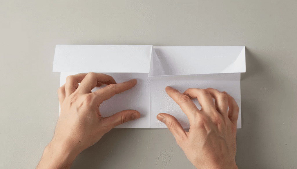 Two hands are skillfully folding a square piece of paper into an asymmetrical origami gift box with a lid attached showcasing the intricate process of creating the base and lid sections The folds create distinct shapes including two triangles as the hands navigate the craft of traditional origami
