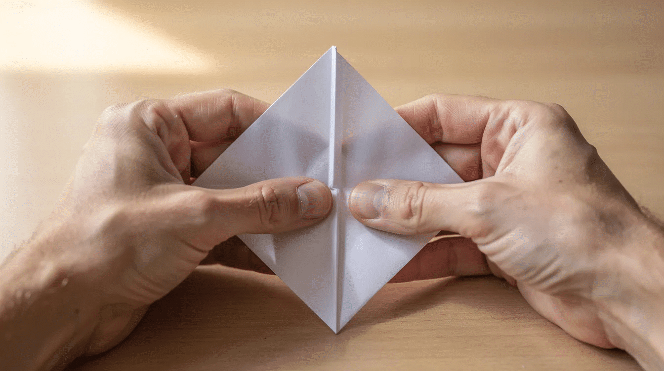 81956a9f e811 44ea ba9f 622ab99f800f The image shows hands gently folding a square piece of paper into a smaller diamond shaped base a crucial step in the traditional origami crane process The fingers are carefully creasing the corners preparing the paper for the next steps in this easy origami tutorial