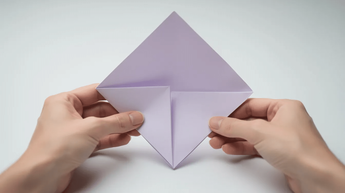 C4cd9d8e 181d 4087 817c 7c50b5888bc3 The image shows a close up of hands carefully lifting the lower flap of a paper base transforming it into a long narrow diamond shape an essential step in creating a traditional origami crane The fingers are positioned to emphasize the crease and the corners of the square piece of paper illustrating the detailed process of this art form